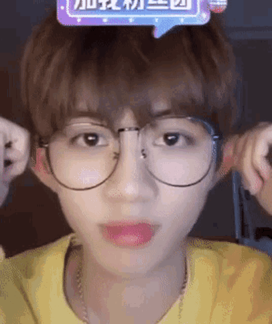 a young man wearing glasses and a yellow shirt with chinese writing on it