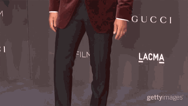 a man in a red tuxedo is standing in front of a wall that says lacma and gucci