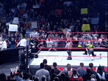 a wrestling match is being played in front of a crowd holding signs including one that says big