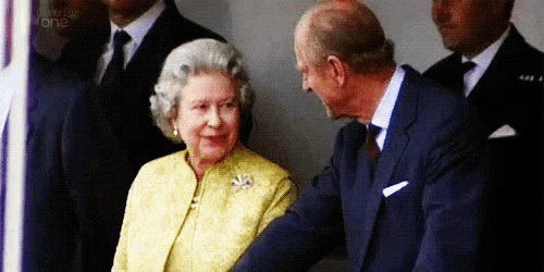 a man in a suit and tie is shaking hands with the queen .