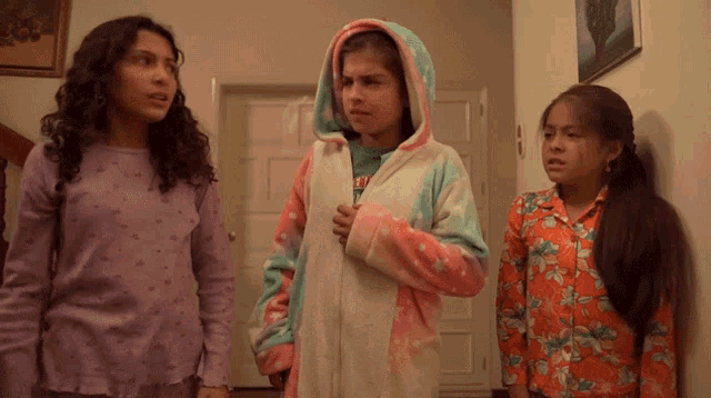 three girls are standing in a hallway and one of them is wearing a unicorn pajama