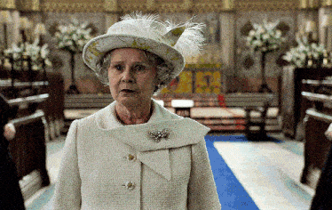 an elderly woman wearing a hat and a white coat stands in a church