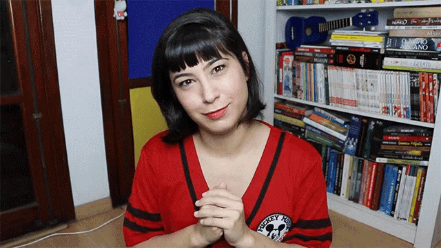 a woman wearing a red mickey mouse shirt is sitting in front of a bookshelf