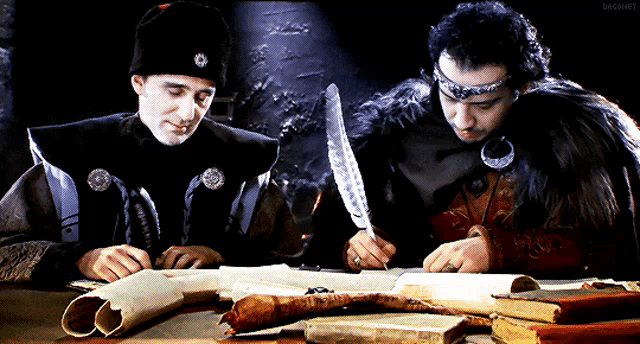 two men are sitting at a table with a feather in their hand and the word bagnet on the bottom