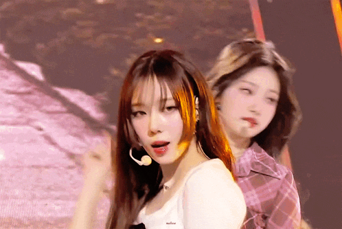 two girls are standing next to each other on a stage and one has a microphone in her ear .