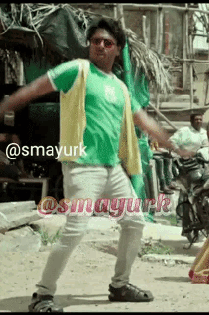 a man in a green shirt is dancing in front of a sign that says @smayurk