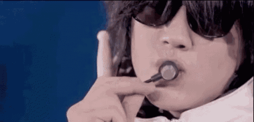 a close up of a person wearing sunglasses and blowing a bubble with a straw .