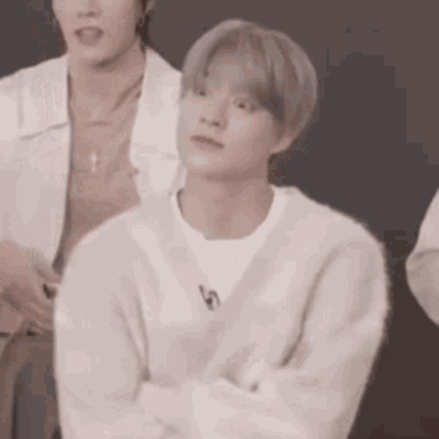 a man in a white sweater is sitting with his arms crossed in front of two other men .