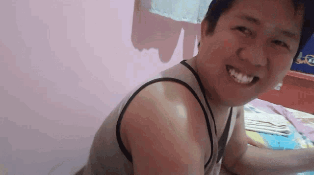 a man wearing a tank top is smiling in front of a pink wall with the letter t on it