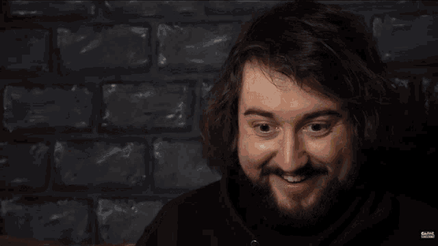 a man with a beard is smiling and has a tattoo on his wrist