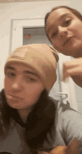 two women wearing beanies are standing next to each other in front of a window .