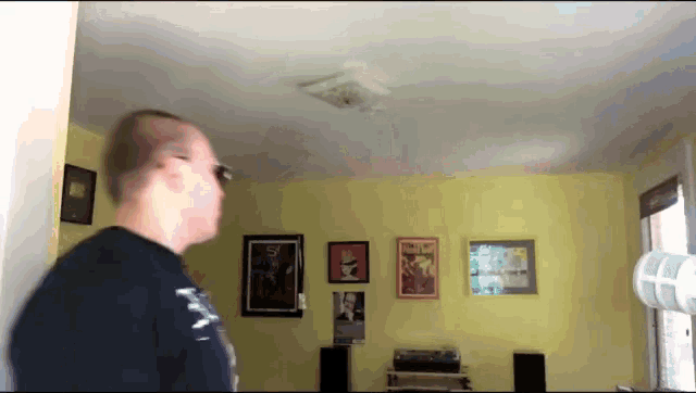 a man in a black shirt is standing in a room with yellow walls and a fan