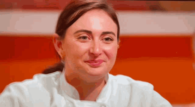 a woman in a white chef 's coat is smiling and looking at the camera .