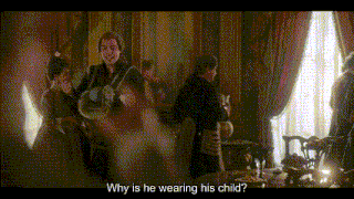 a group of people are standing around a table with a man asking why is he wearing his child .
