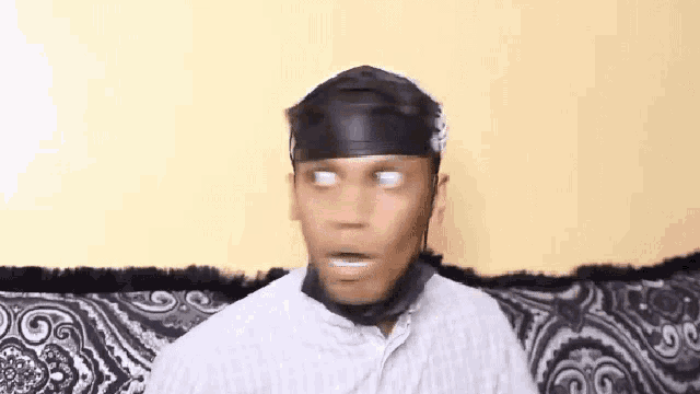 a man wearing a black headband is sitting on a couch making a funny face .