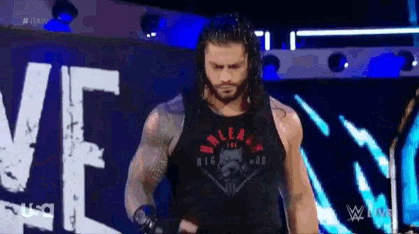 roman reigns is standing on a stage in front of a sign that says wwe live .