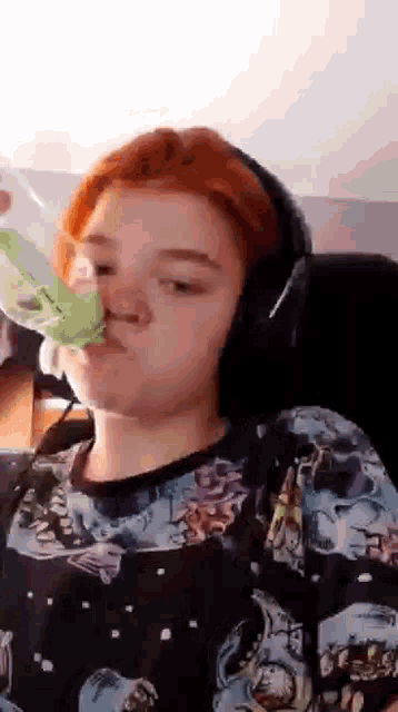 a person with red hair is wearing headphones and drinking from a plastic bottle .