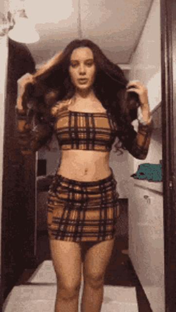 a woman wearing a plaid top and skirt is standing in a hallway