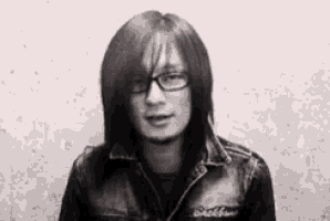 a man with long hair and glasses is wearing a leather jacket