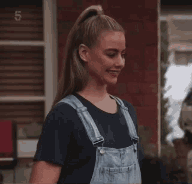 a woman wearing overalls and a black shirt with the number 5 on the bottom right