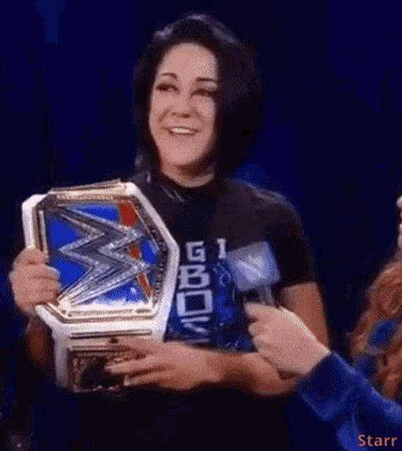 a woman wearing a black shirt that says git on it holds a wrestling championship belt