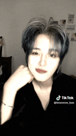 a woman with blue hair is making a face with her hand on her chin