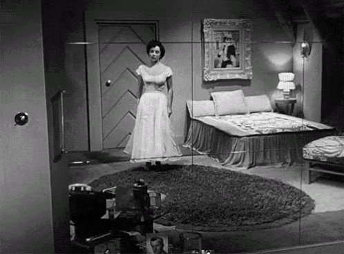 a woman in a white dress stands in front of a bed in a bedroom