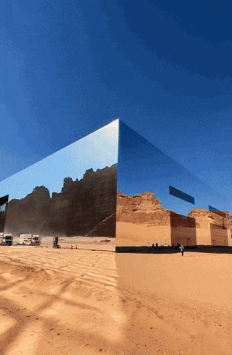 a mirrored building in the middle of a desert with mountains reflected in it
