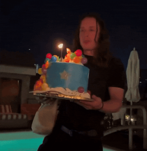 a man is holding a blue cake with balloons on top