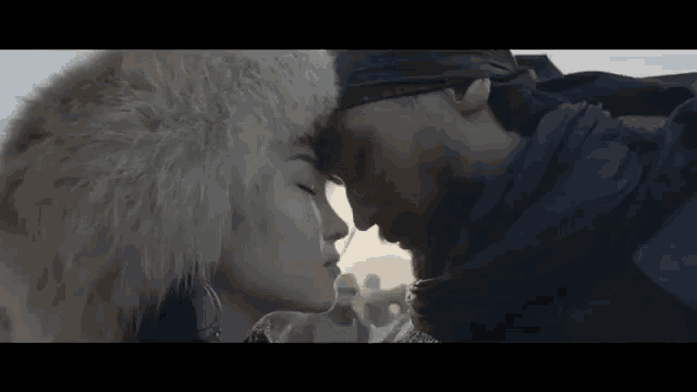 a man and a woman are kissing each other in the desert . the woman is wearing a fur hat .
