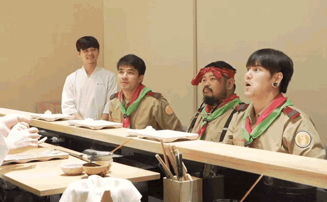 a group of men are sitting at a table with one wearing a bandana that says ' a ' on it