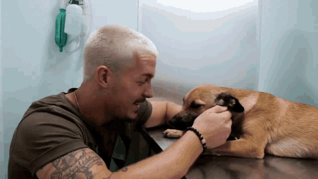 a man with a tattoo on his arm looks at a brown dog