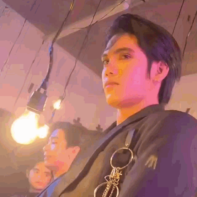 a man in a black jacket is sitting in front of a light bulb .