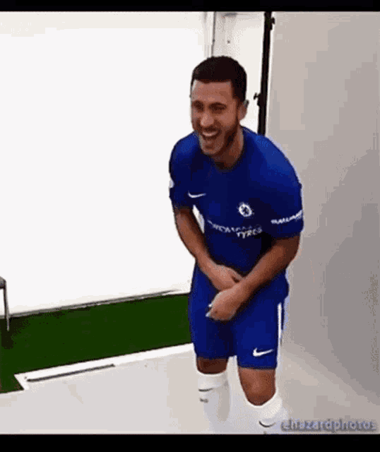 a man in a blue shirt and shorts is laughing while holding his pants in a room .