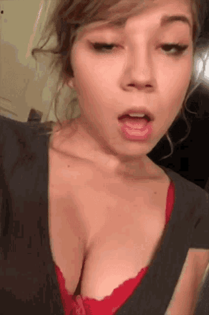 a woman in a red bra and a gray shirt is taking a selfie .