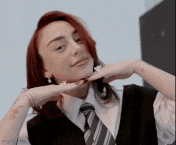 a woman with red hair is wearing a black vest and tie .
