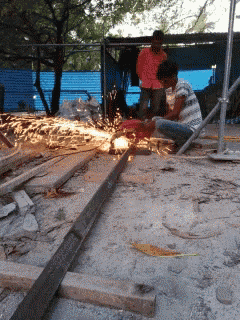 a man is cutting a piece of metal while another man watches