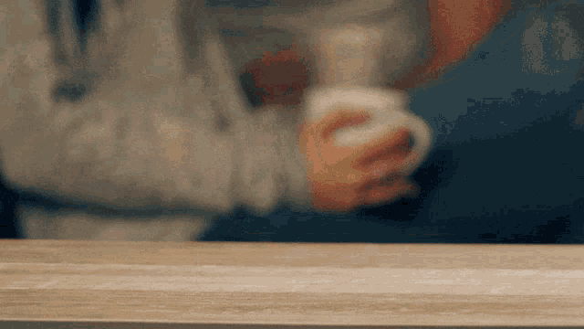 a person sitting at a table holding a white mug