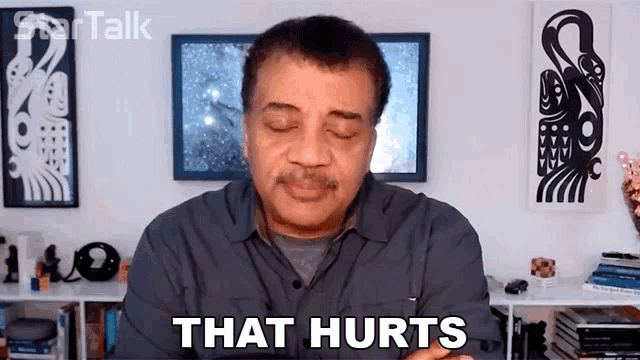 a man with his eyes closed says that hurts in front of a wall with pictures on it