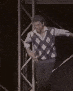 a man in a plaid vest is dancing on a stage in front of a microphone .