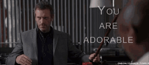 a man in a suit holds a red object in front of a sign that says you are adorable