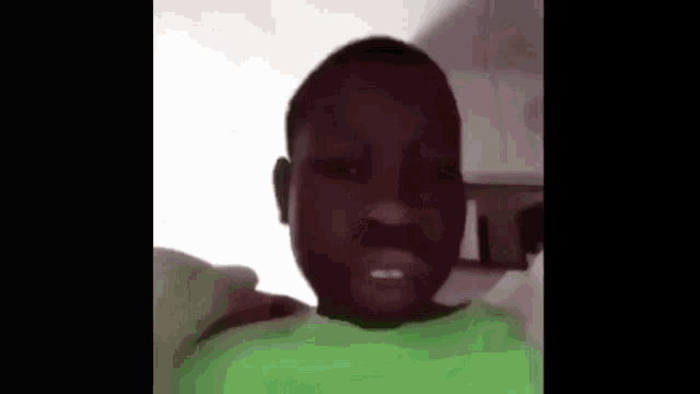 a young boy in a green shirt is making a funny face while looking at the camera .