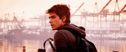 a man wearing headphones and a backpack is standing in front of a large body of water .