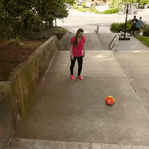 a girl in a pink shirt is kicking a soccer ball on a sidewalk