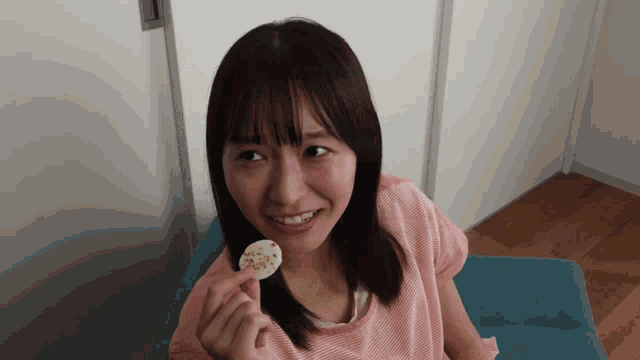 a woman in a pink shirt is smiling while holding a piece of food in her hand