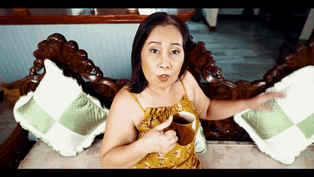 a woman is sitting on a couch holding a cup and pointing at it