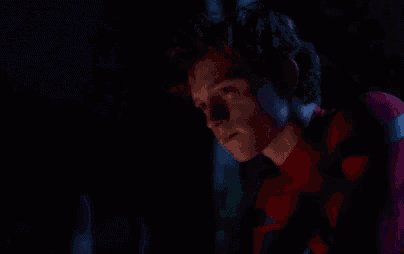 a young man in a spiderman costume is looking at a computer screen at night .
