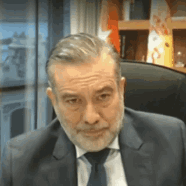 a man with a beard wearing a suit and tie looks at the camera