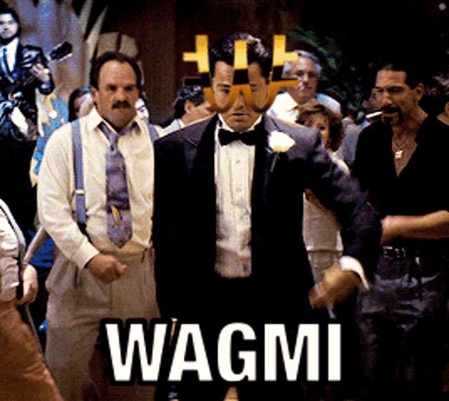 a man in a tuxedo stands in front of a crowd with the word wagmi on the bottom