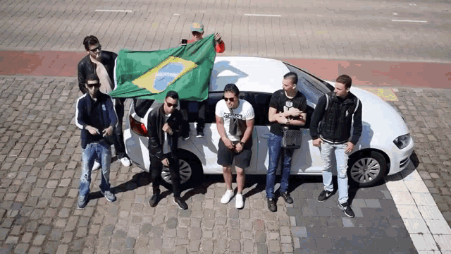 a group of men standing in front of a white car with a man holding a brazilian flag